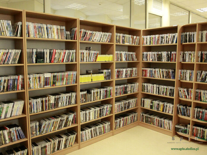 Drewniane regały w bibliotece wypełnione po brzegi pudełkami z płyłami DVD i CD