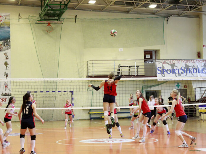 Siatkarka w czerwonej koszulce wyskakuje do piłki nad siatką podczas meczu w hali sportowej