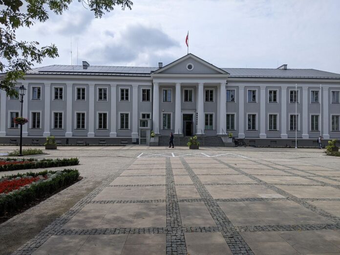 Duży, szary, dwukondygnacyjny budynek z czterema kolumnami