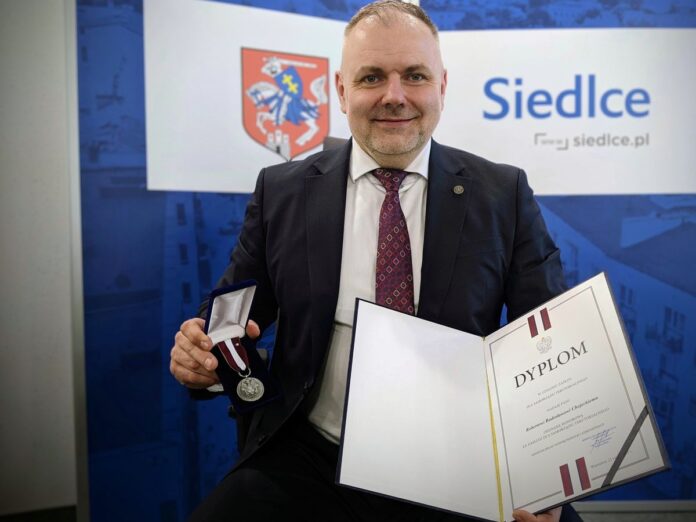 Uśmiechnięty mężczyzna w garniturze z dyplomem w ręku