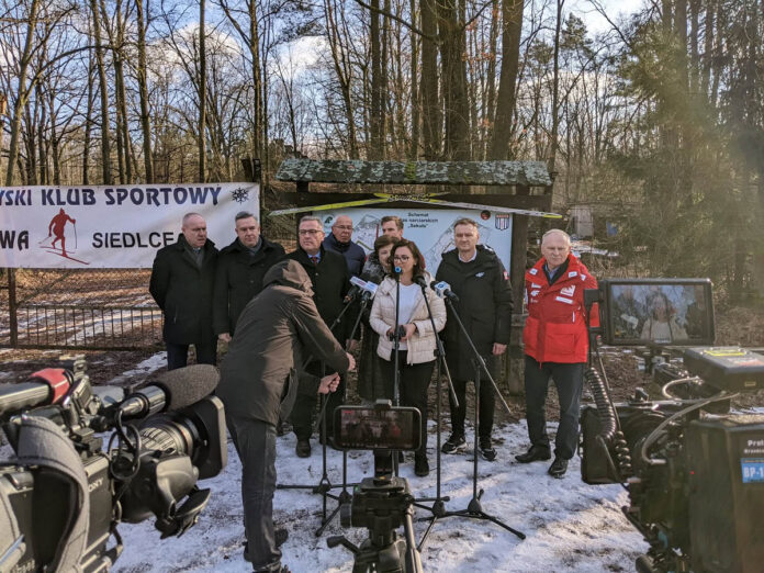 Konferencja prasowa grupy osób w lesie w zimowej scenerii.