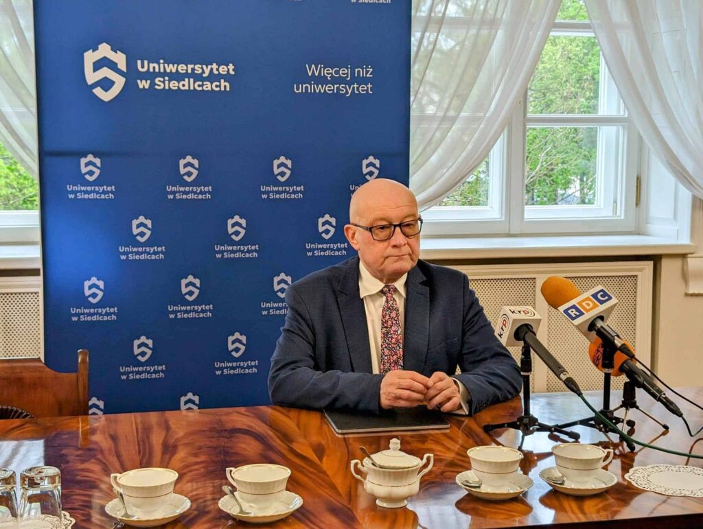 Mężczyzna siedzący za stołem przed mikrofonami.