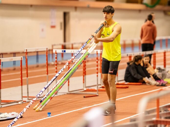 Młody sportowiec w żółto-czarnym stroju przygotowuje się do skoku o tyczce