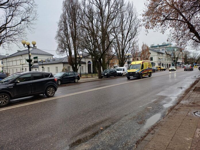 Ulica z samochodami i karetkami, tworzącymi ruchliwą scenę miejską.