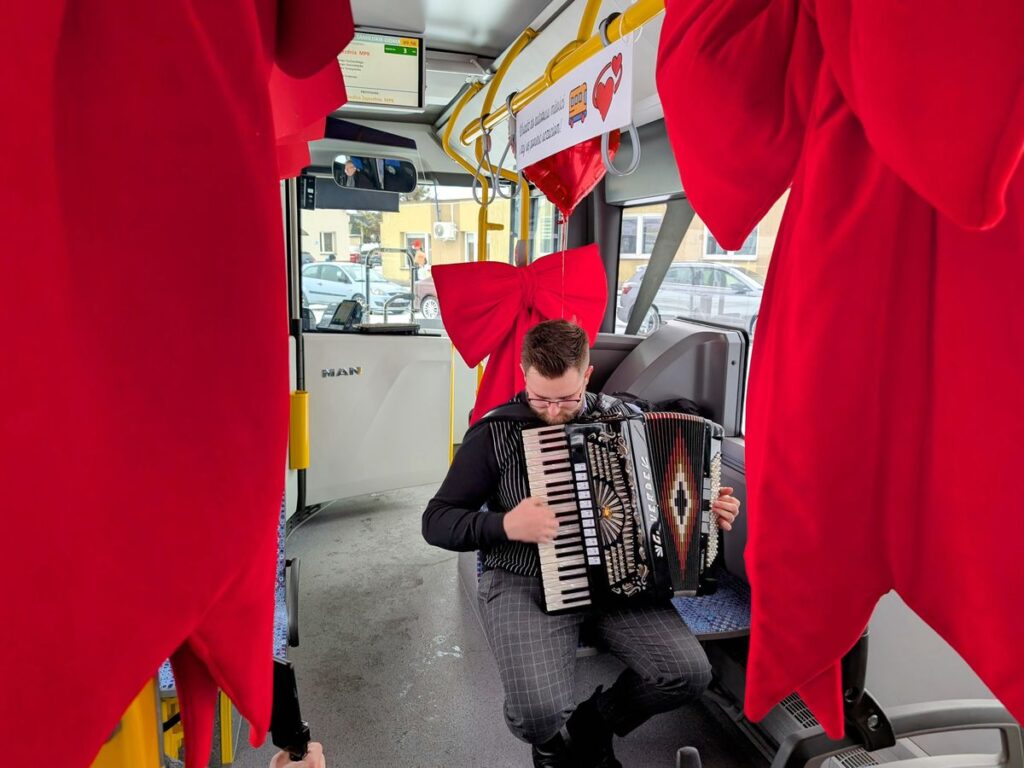 Akordeonista we wnętrzu autobusu gra w otoczeniu czerwonych wstążek i serc