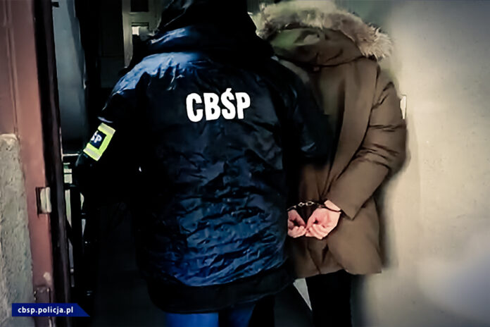 Policjant prowadzi zatrzymanego mężczyznę z kajdankach