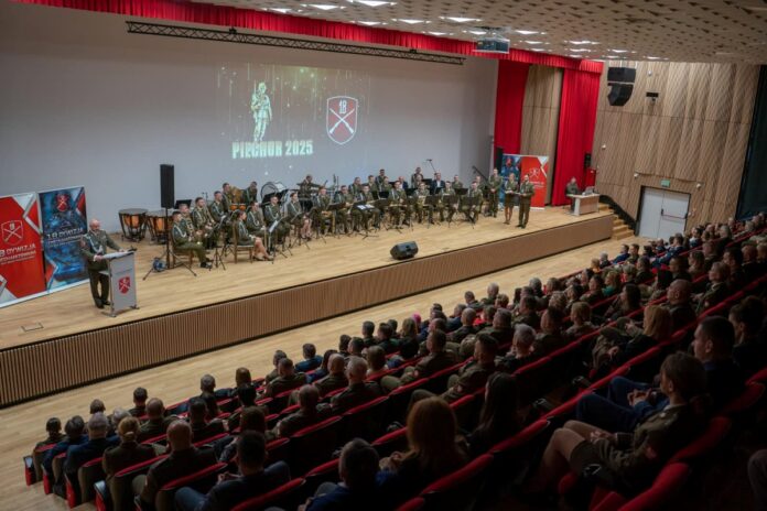 Duża sala audytoryjna z ludźmi siedzącymi na krzesłach, skupionymi na wydarzeniu na scenie.