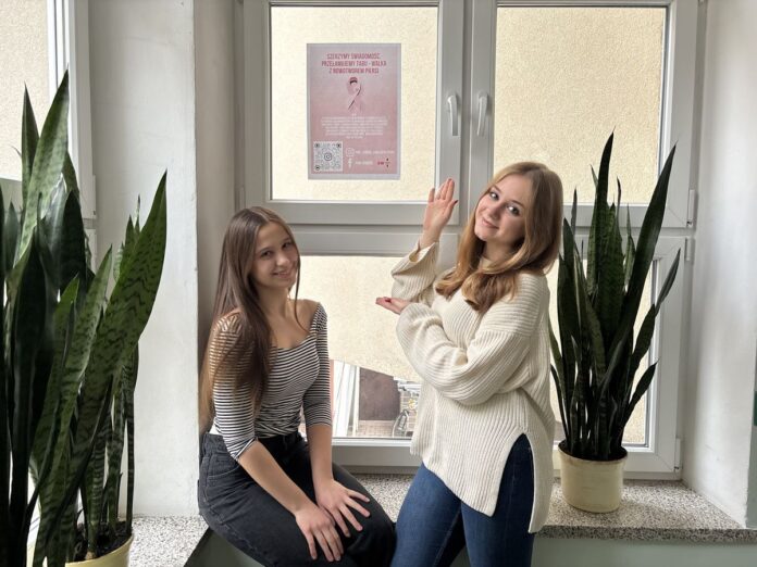 Dwie dziewczynki siedzą na parapecie okna, obok nich plakat, tworząc przytulną atmosferę w pomieszczeniu.