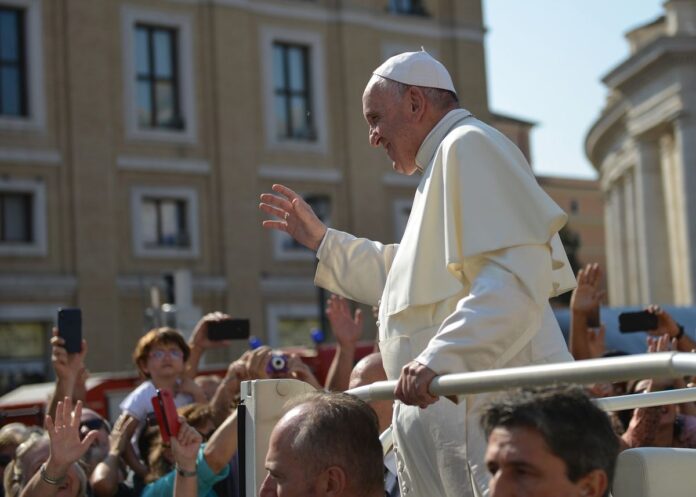 Papież Franciszek macha do tłumu, witając wiernych.