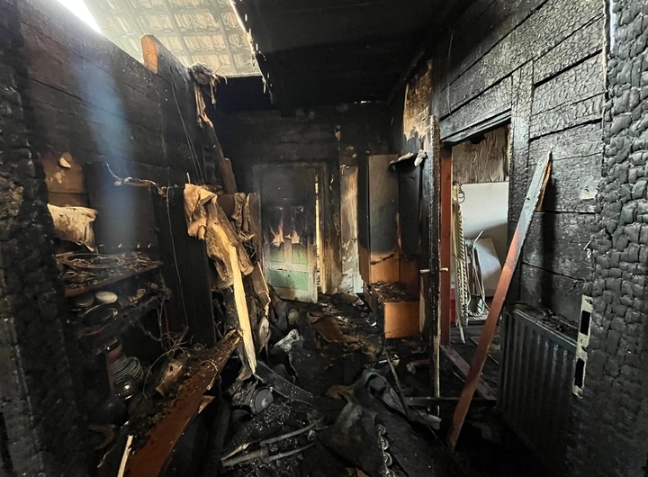 . Wnętrze spalonego domu z widocznym kominkiem, zniszczone ściany i popioły na podłodze.