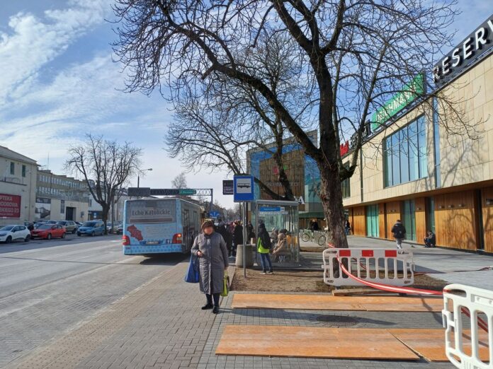 Tętniąca życiem ulica z przechodniami i przystankiem autobusowym, ukazująca codzienne życie w mieście.