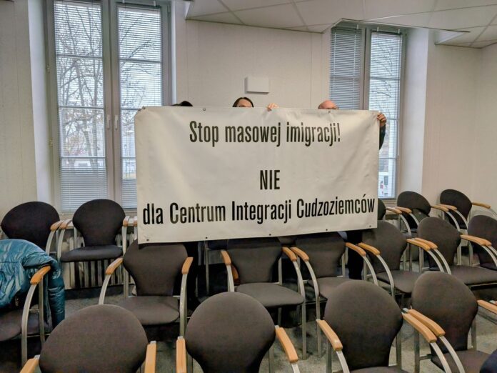 Grupa osób w pomieszczeniu trzyma baner z napisem 