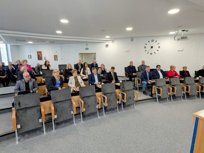 Grupa osób siedząca w dużej sali.