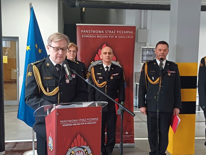Zespół mężczyzn w mundurach stoi przy podium, reprezentując instytucję w oficjalnym kontekście.