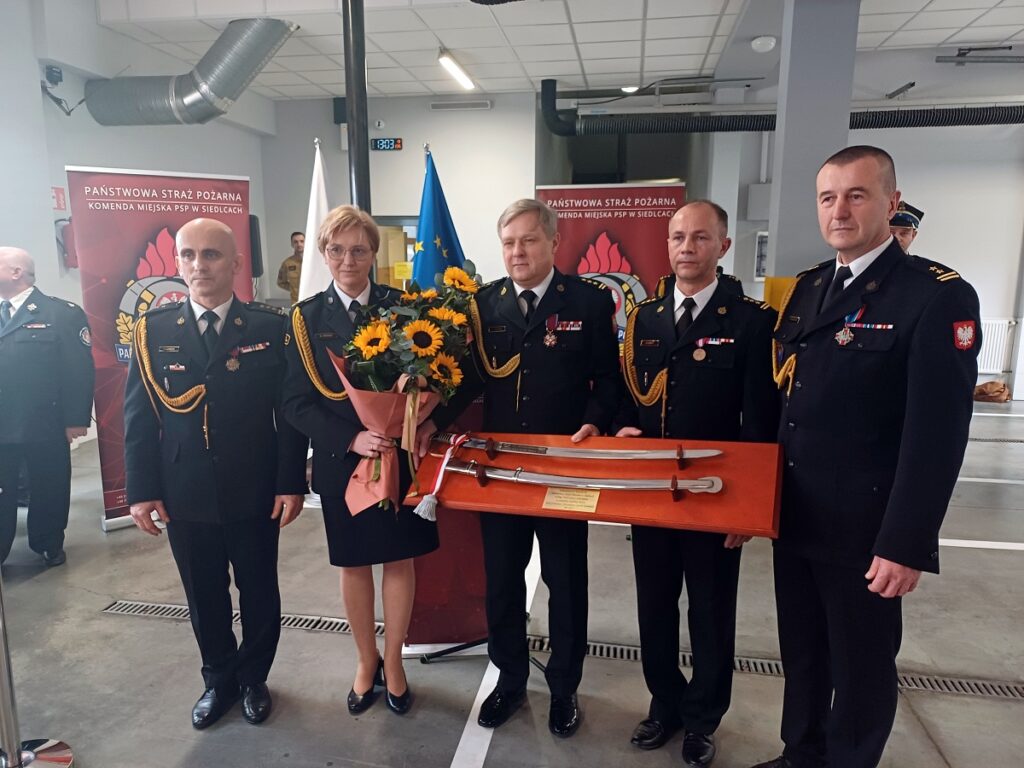 Grupa osób w mundurach trzymająca prezent, prezentująca współpracę i zaangażowanie