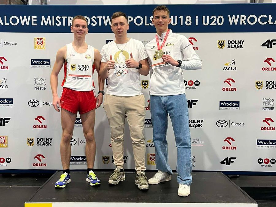 Trzej mężczyźni szczęśliwi - jeden z nich prezentuje złoty medal.