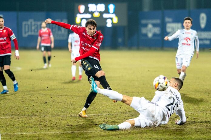 Piłkarz próbuje kopnąć piłkę na boisku, skupiony na wykonaniu precyzyjnego strzału.