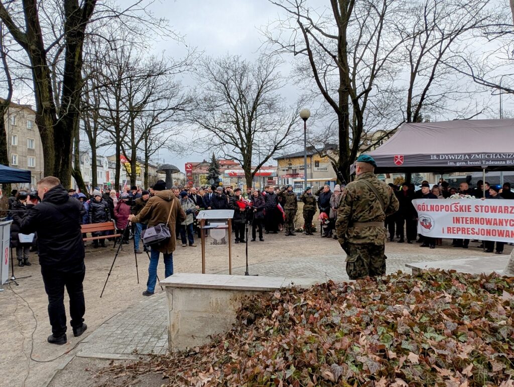 Grupa ludzi zgromadzona przy pomniku podczas patriotycznego święta
