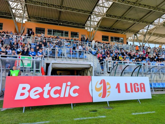 Napis Betclic 1 Liga na banerze przed wejściem na stadion piłkarski.