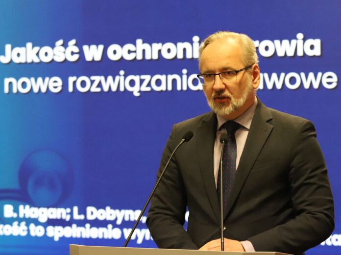 Siwiejący mężczyzna w czarnej marynarce stoi przed mikrofonem.