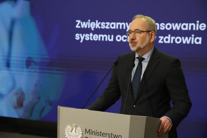 Siwiejący mężczyzna w czarnej marynarce stoi przed mikrofonem.