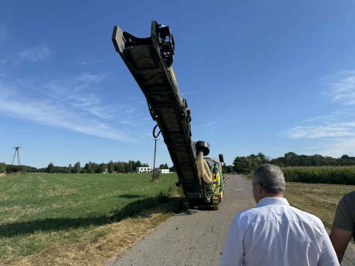 Maszyna do robót budowlanych stojąca na drodze między terenami zielonymi.