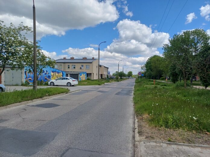 Zniszczona nawierzchnia ulicy w mieście z samochodami i budynkami w tle.