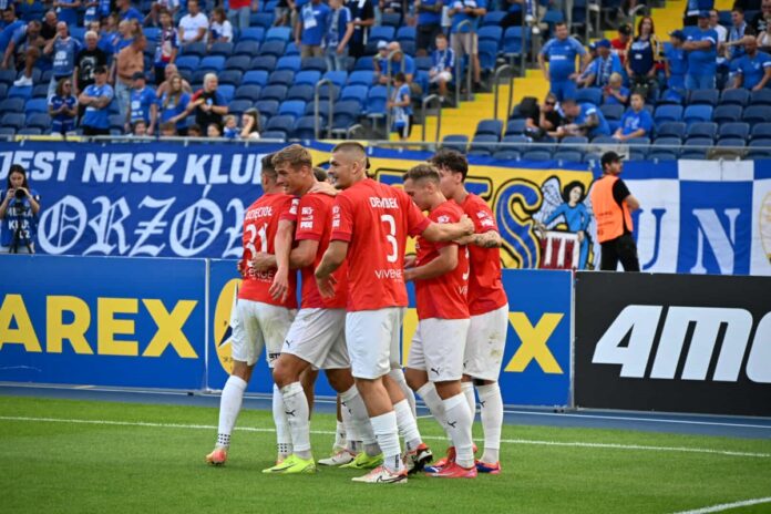 Grupa piłkarzy zbiera się w huddle na boisku, omawiając strategię przed rozpoczęciem meczu.