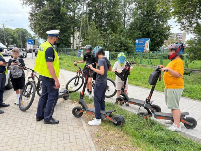 Policjanci stoją w grupie razem z osobami na hulajnogach elektrycznych.