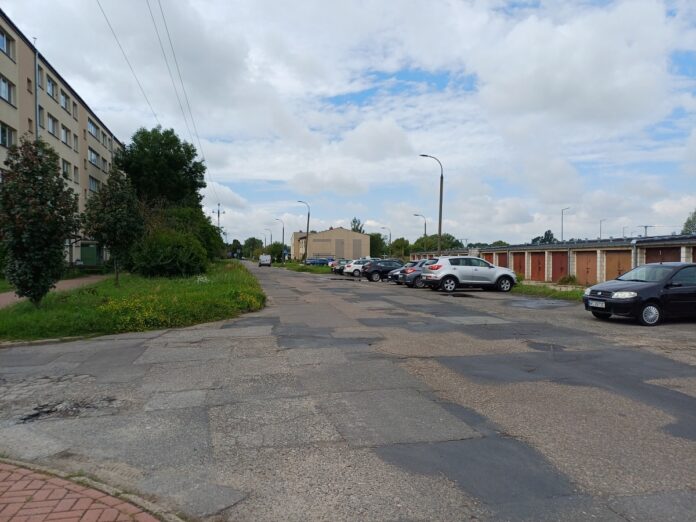 Zniszczona nawierzchnia ulicy w mieście z samochodami w tle.