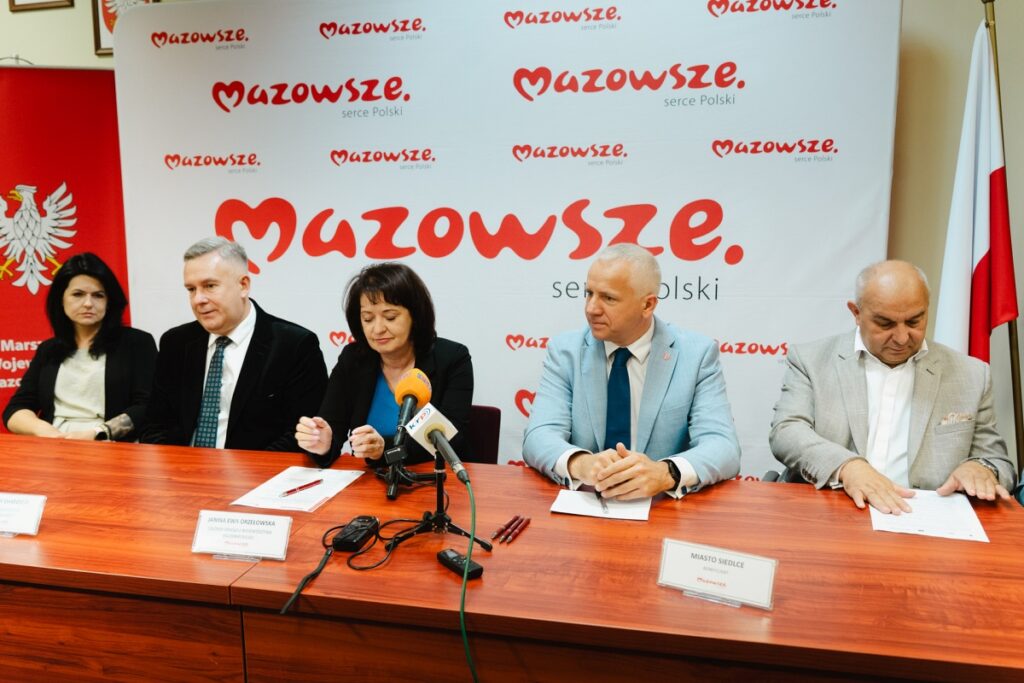 Grupa osób siedzi przy stole przed mikrofonami
