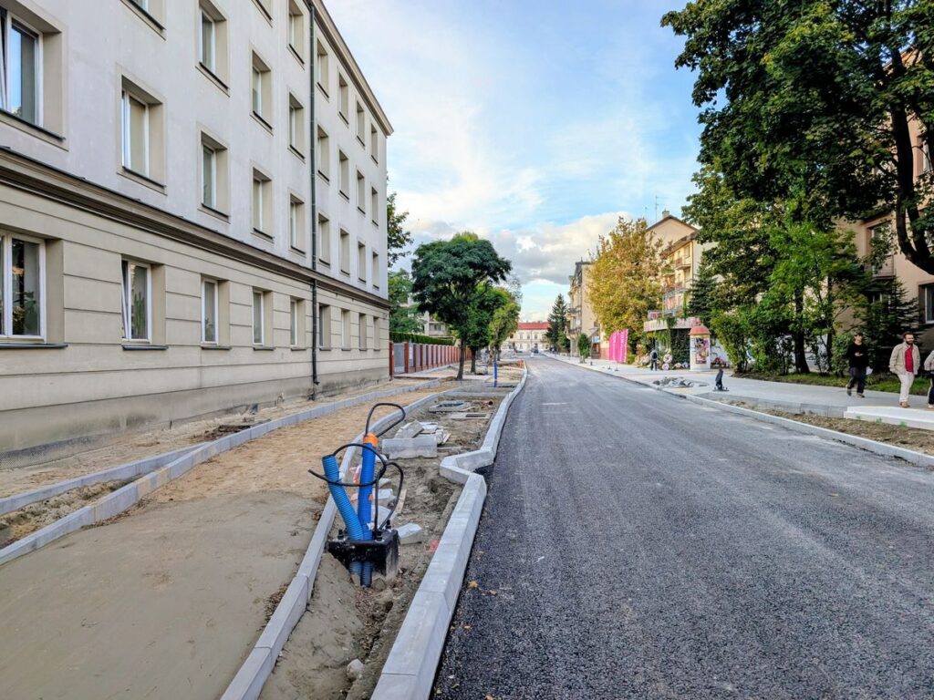 Budowa drogi miejskiej. Widać nową nawierzchnię i prace przy ciągu pieszo-rowerowym. 
