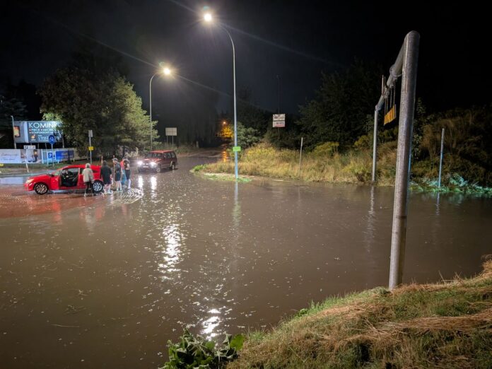 Ulica zalana brudną wodą pośrodku stoją samochody.