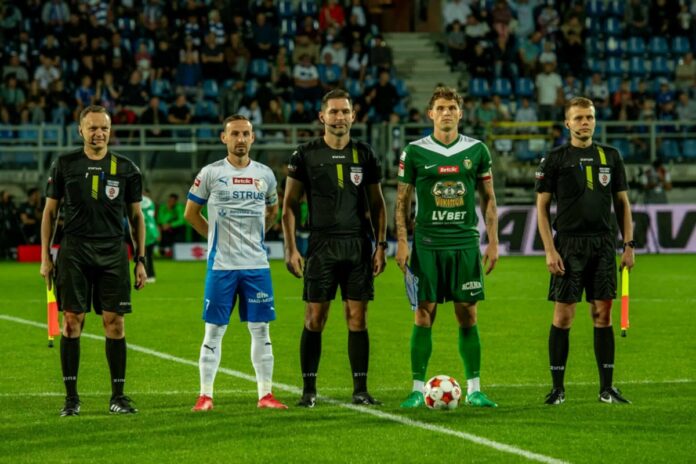 Pięciu mężczyzn stoi na boisku piłkarskim, na murawie leży piłka