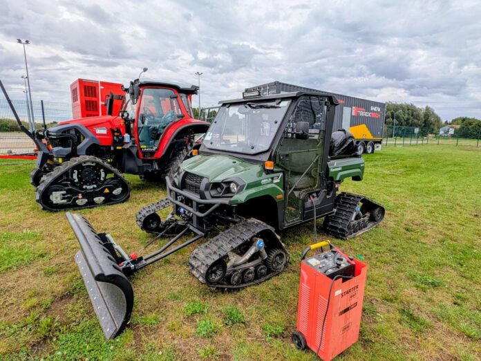 Dwa traktory z pługiem i przyczepą zaparkowane na trawie.