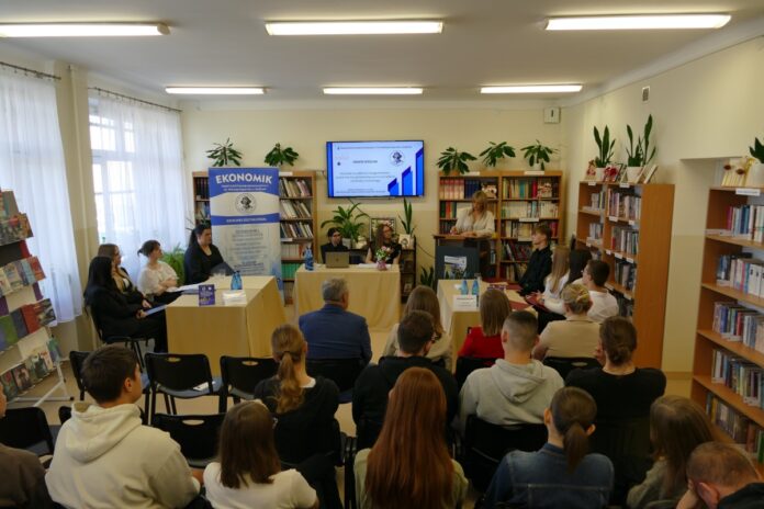 Grupa ludzi siedzi w pokoju otoczona książkami, prowadząc dyskusję w przyjaznej atmosferze.