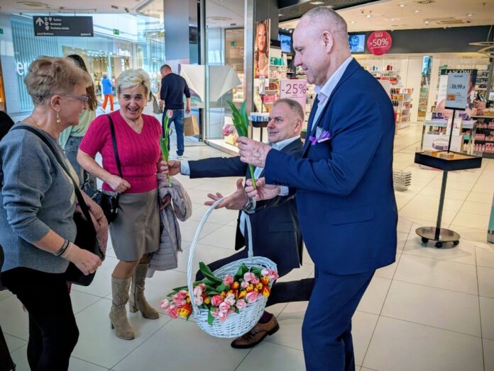 Mężczyzna w eleganckim garniturze ofiarowuje kwiaty ludziom.