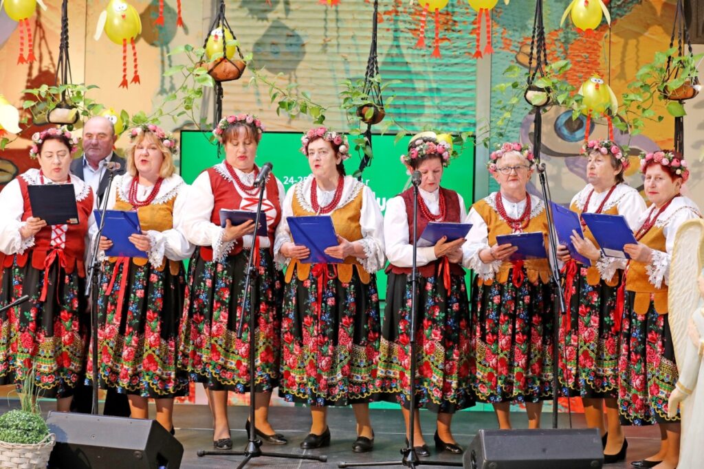 Grupa ludzi w tradycyjnych strojach śpiewa, tworząc radosną atmosferę podczas lokalnego wydarzenia kulturalnego.
