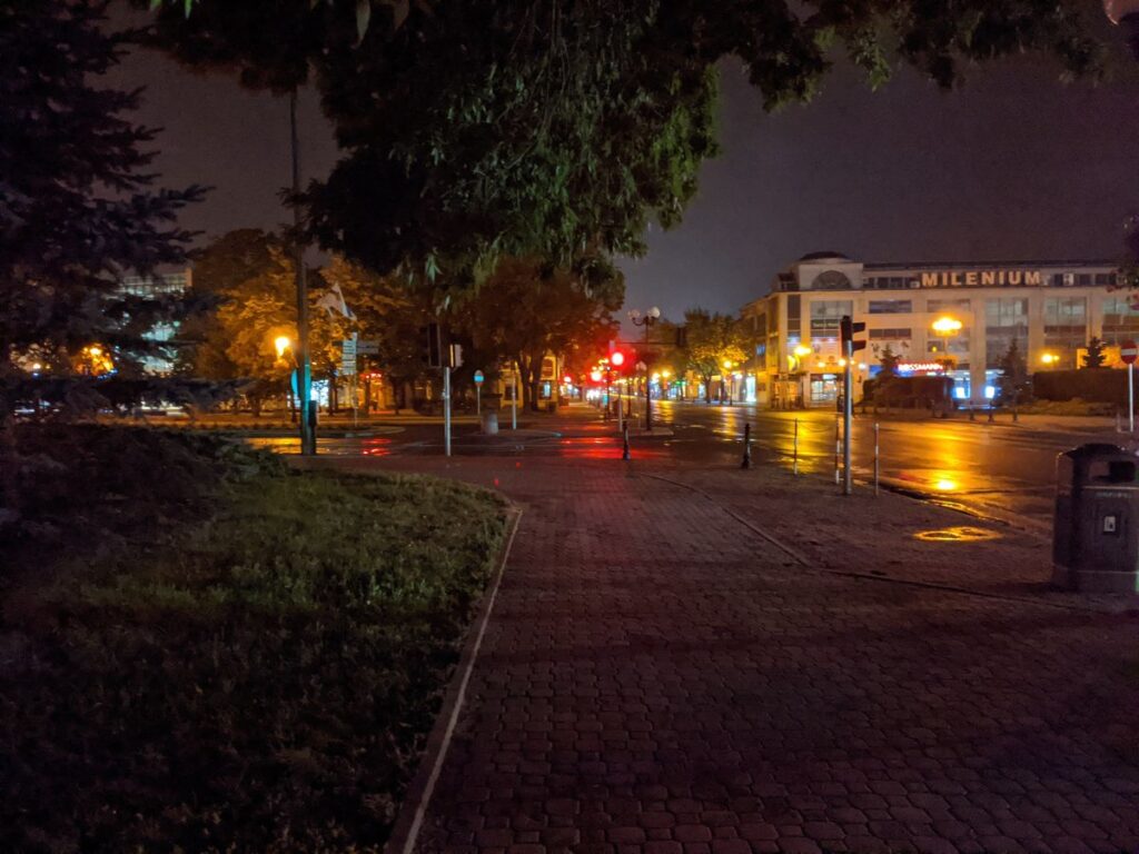 Nocne zdjęcie ulicy w mieście z budynkami i samochodami w tle.
