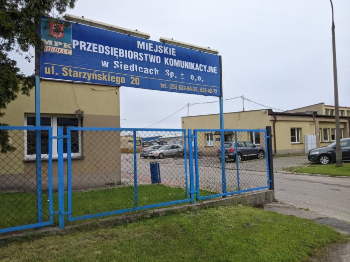 Parterowy budynek ogrodzony niebieską siatką z napisem Miejskie Przedsiębiorstwo Komunikacyjne w Siedlcach