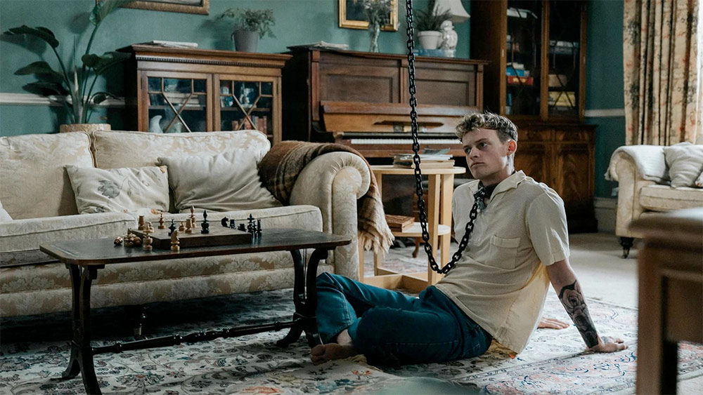 Mężczyzna siedzi na podłodze w salonie, otoczony meblami i dekoracjami.