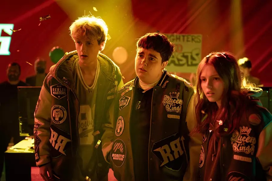 Troje młodych ludzi stoi przed sceną, uśmiechając się i rozmawiając ze sobą.