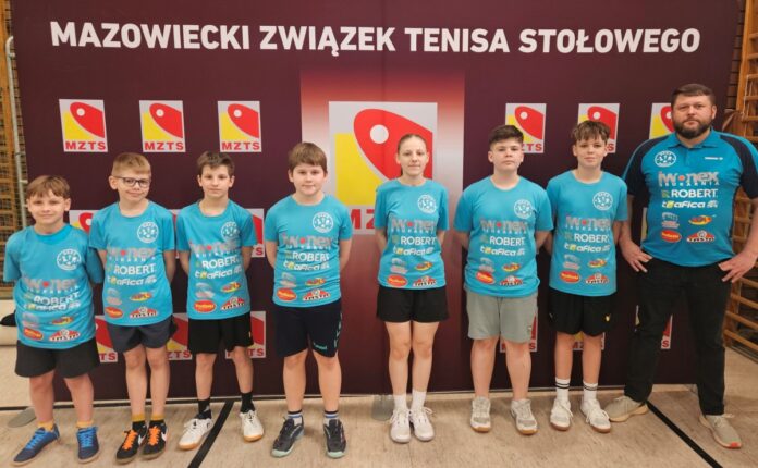 Grupa młodych chłopców i dziewcząt w niebieskich koszulach, uśmiechających się do kamery.