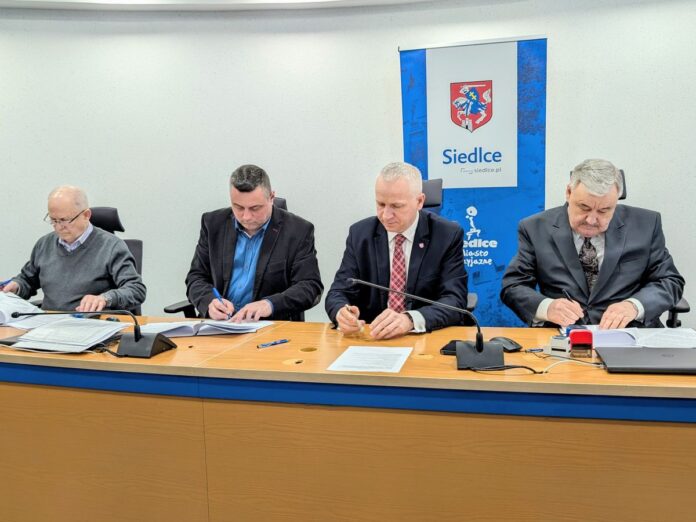 Czterej mężczyźni siedząc za stołem konferencyjnym podpisują umowy.