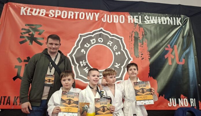 Grupa dzieci pozująca z trofeami, uśmiechnięta i dumna z osiągnięć.