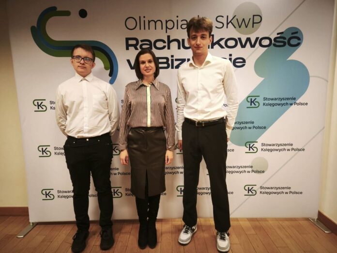 Trzy osoby stoją przed banerem