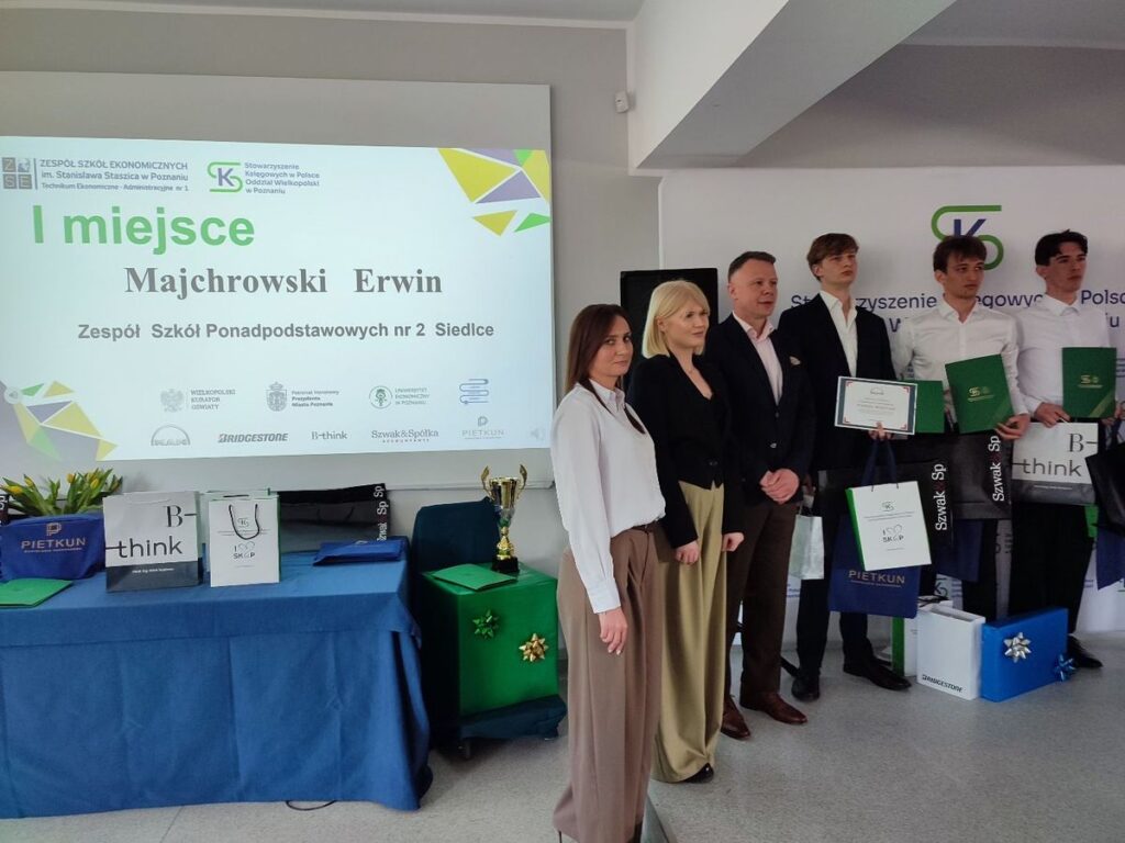 Grupa laureatów konkursu uśmiechają się, trzymając nagrody na tle dekoracyjnej sceny.