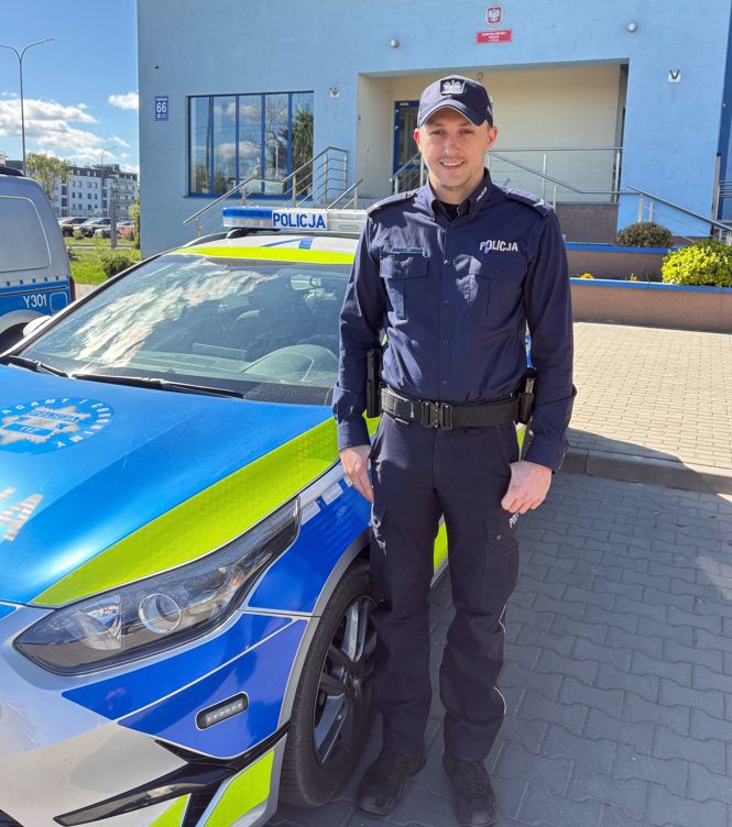 Mężczyzna w mundurze stoi obok radiowozu policyjnego.