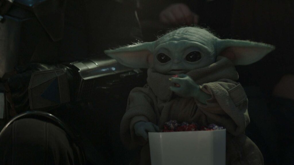 Mały Yoda trzyma popcorn, uważnie oglądając film.