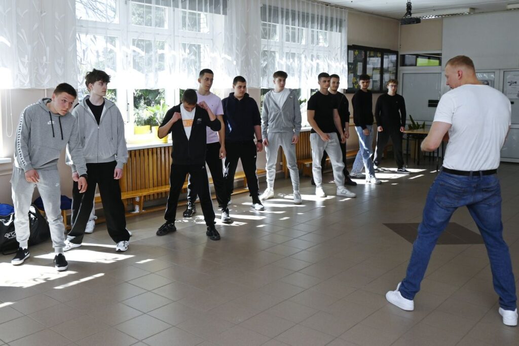 Grupa mężczyzn stoi w linii w pomieszczeniu, wszyscy zwróceni w stronę obiektywu.